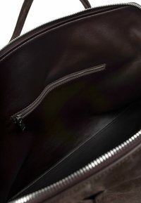 Wnętrze brązowej skórzanej torby z kieszenią na zamek. Gładka faktura i ciemny, jednolity kolor. Z metalowym zamkiem błyskawicznym.