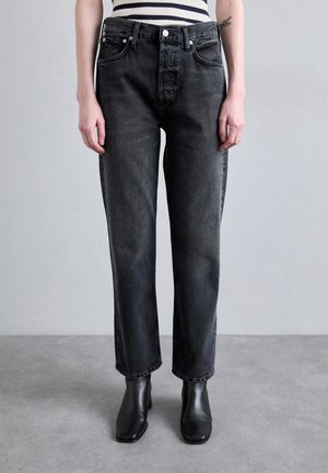 Jeans de mezclilla negra con corte recto, que cuentan con cinco bolsillos, botones plateados y un leve desgastado. Combinados con botas negras hasta el tobillo.