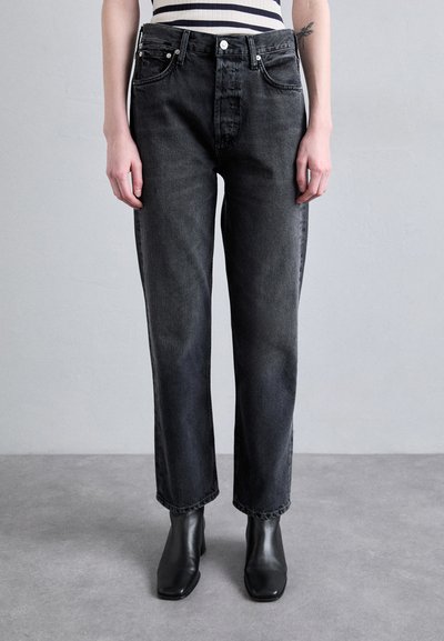 Jean en denim noir avec une coupe droite, comportant cinq poches, des boutons en argent et un léger effet délavé. Associé à des bottines noires.