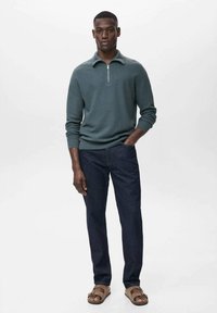 Light green zip-up sweater, dark blue jeans, and beige sandals. Smooth texture, fitted design, with a stand-up collar and ribbed cuffs.