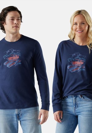 Meripinkan t-shirt lengan panjang navy yang terbuat dari kapas, menampilkan grafik pusat dari snowcat dan pegunungan dalam nuansa merah dan biru.