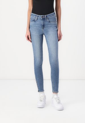 Smala jeans i ljusblå denim med hög midja, frampocketar och lätt slitage vid fållen. I kombination med vita sneakers.