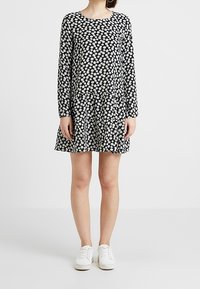 Schwarzes langärmliges Kleid mit weißem Blumenmuster, ausgestelltem Saum und rundem Ausschnitt, getragen mit weißen Sneakers. Weicher Stoff.