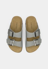 Γκρι σουέντ σανδάλια με δύο ρυθμιζόμενες ιμάντες και ασημένιους μανταλάκια. Η επιφάνεια του παπουτσιού είναι ανοιχτό καφέ, αναδεικνύοντας μια μαλακή υφή και μινιμαλιστικό σχέδιο.