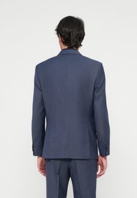 Giacca di completo blu scuro su misura con colletto a scollo, apertura centrale e polsini con bottone. Realizzata in tessuto testurizzato, progettata per un look aderente.