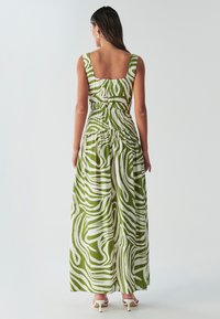 Robe maxi verte et blanche avec décolleté carré, sans manches, taille cintrée et motif abstrait en tourbillon. Tissu lisse et léger.