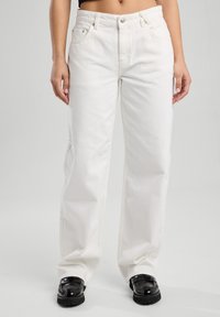 White denim pants with a loose fit, featuring a button closure, belt loops, and front pockets. The fabric has a smooth texture.
