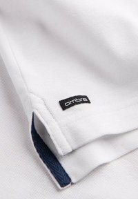 Bílá polokošile s texturovanou tkaninou, obsahující černou "ombre" nášivku a námořnickou modrou accentaci na lemu. Čistý design a volný střih.