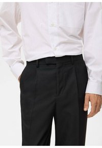 Witte en roze gestreepte overhemd met knopen, gecombineerd met op maat gemaakte zwarte pantalon met zijzakken en een aansluitende tailleband.