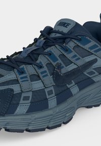 Κοντινό πλάνο μπλε αθλητικού παπουτσιού Nike που δείχνει πολυεπίπεδες υφές, κορδόνια, ραμμένες επικαλύψεις και το λογότυπο Nike swoosh στο πλάι.