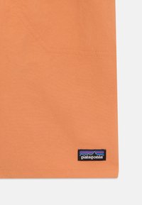Narančasta majica s kratkim rukavima glatke teksture, s malim logotipom Patagonia pri rubu i suptilnim šavnim detaljima.