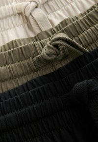 Tre par shorts i beige, olivgrön och svart, med elastiska midjeband och knutna dragsnören samt en rynkad tygtextur.