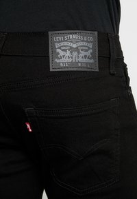 Jeans Levi's 511 negros usados, mostrando el bolsillo trasero con la etiqueta roja de Levi's y la parcha de cuero con el logo de dos caballos y talla W31 L.