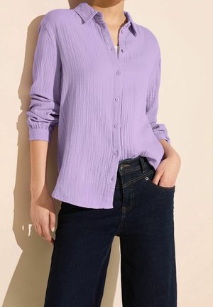 Lichtpaarse button-up shirt met een textuurstof en kreukelige uitstraling, met opgerolde mouwen, gecombineerd met donkerblauwe denim jeans. Eenvoudige designelementen.