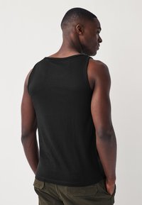 Sort bomulds-tanktop med rund halsudskæring og brede skulderstropper. Glat tekstur, få syninger og tætsiddende design.