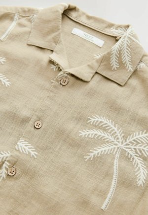 Chemise beige à manches courtes en lin avec des motifs de palmiers brodés en blanc, dotée d'un col et de boutons de fermeture.