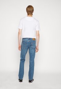 Blå denimjeans med rak passform, med en brun läderlappar på den bakre midjebandet och diskreta sömmar på fickorna.