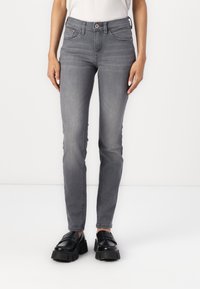 Jeans de mezclilla gris con un diseño ajustado, cinco bolsillos y cremallera. Textura suave con un ligero elasticidad, combinados con zapatos negros gruesos.