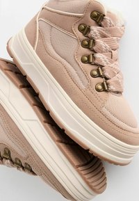 Sneaker alte rosa realizzate in materiali scamosciati e in rete, con occhielli in metallo, lacci decorati e suole in gomma spessa e texture.