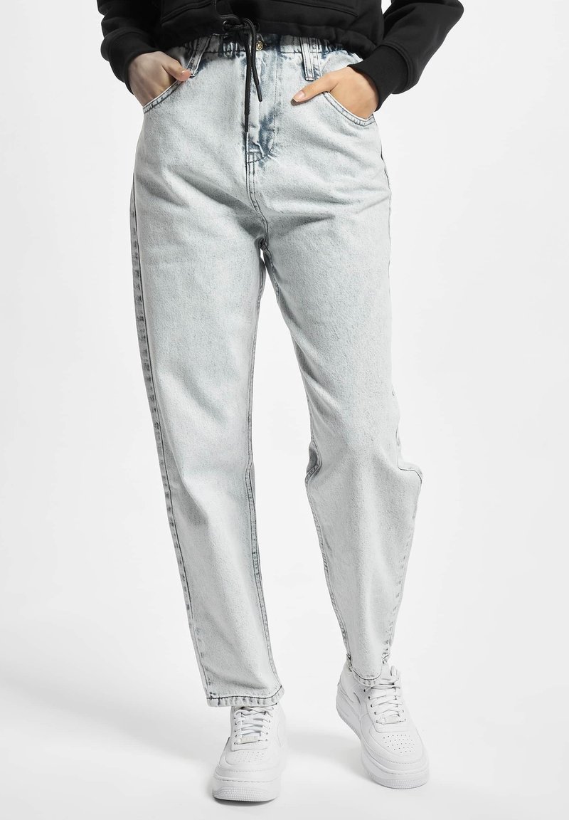 Jeans in denim chiaro con vestibilità dritta, caratterizzati da vita alta, strisce laterali e tasche anteriori. Abbinati a sneaker bianche.