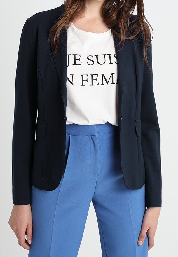 Marinblå blazer med skräddarsydd passform, två framfickor, lagd över en vit t-shirt med svart text, kombinerad med ljusblå byxor.