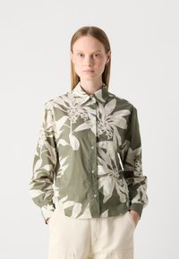 Chemise à manches longues en vert olive avec un imprimé floral blanc, devant boutonné, col pointu et coupe décontractée. Tissu texturé.