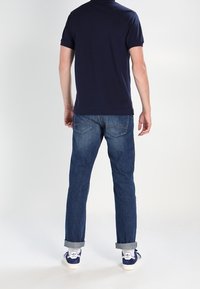 Navy t-paita lyhyillä hihoilla, yhdistettynä vaaleansinisiin farkkuihin, joissa on käännetyt hihansuut, viimeistelty valkoisilla lenkkareilla, joissa on sinisiä yksityiskohtia.