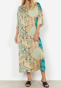 Pitkä, monivärinen mekko, jossa väljä istuvuus. Ominaisuuksiin kuuluu sekoitus merensinistä, oranssia ja beigeä kuvioita; v-kaula-aukko ja lyhyet hihat; sileä kangas.