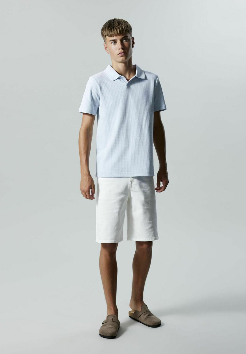 Ljusblå ribbad kortärmad polo, vita shorts och bruna slip-on skor. Enkelt mönster med klassisk krage.