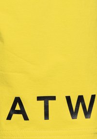 Geel stof met grote zwarte letters "A T W" gedrukt nabij de onderrand.