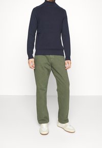 Marinblå ribbad polotröja med åtsittande ärmslut, matchad med olivgröna raka byxor och vita sneakers med beige detaljer.