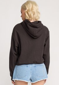 Hoodie court marron avec capuche, manches longues et poignets côtelés, associé à un short en denim déchiré bleu clair.