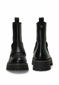 Botines negros de cuero con un upper texturizado, paneles laterales elásticos y una suela robusta de tacos. Presentan una correa en la parte frontal con un acento metálico.