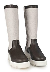 Sección de tobillo de cuero marrón y parte superior sintética acolchada color crema, con una suela blanca gruesa y detalle de cremallera lateral.