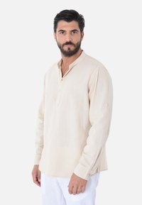 Camicia beige a maniche lunghe con scollo henley e patta con bottoni, realizzata in tessuto leggero, con una vestibilità comoda e dettagli ai polsini.