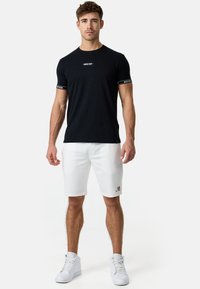 Sort bomulds T-shirt med korte ærmer, prydet med hvidt logo, parret med hvide shorts og hvide sneakers. Standard atletisk pasform.