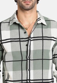 Camicia a quadri verde e bianca con accenti neri, dotata di colletto e bottoni visibili. Tessuto testurizzato, design informale.