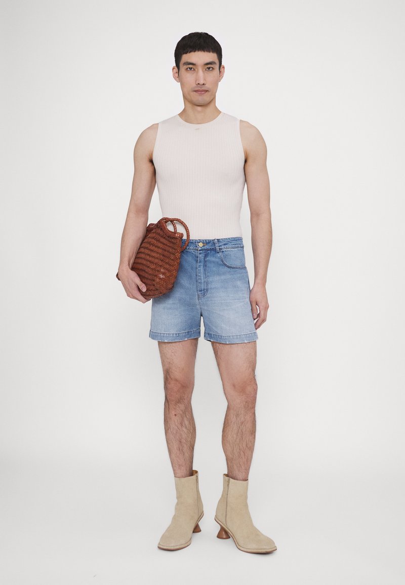 Haut sans manches côtelé rose clair, shorts en denim bleu, bottines beiges à hauteur de cheville et un sac tissé marron avec des anses, posé sur un fond blanc.