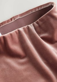 Detailní záběr na měkkou sametovou látku v jemně růžové barvě s elastickým páskem a hladkým podšívkem uvnitř.