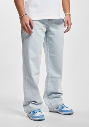 Jeans de mezclilla azul claro con un corte holgado, remangados en la parte inferior, combinados con zapatillas azul y blanca con un diseño de cordones.