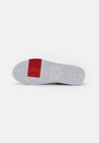 Semelle de sneaker blanche avec un accent rouge, motif de grip texturé et marquage. Présente un design de semelle en zigzag pour une meilleure adhérence.