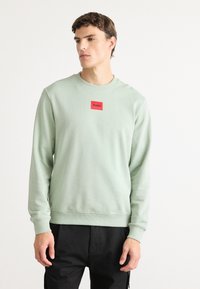 Felpa verde menta realizzata in morbido tessuto, con scollo rotondo e polsini a costine. Sulla parte frontale c'è un piccolo etichetta quadrata rossa con la scritta "HUGO".