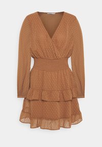 Robe portefeuille marron à pois avec une taille smockée, des manches longues et un ourlet à volants. Réalisée en tissu léger et texturé.