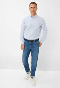 Camicia a righe blu chiaro con bottoni abbinata a jeans blu e sneakers bianche. Vestibilità slim con una leggera texture, maniche arrotolate e una cintura.