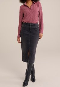 Jupe en denim gris avec une fente à l'avant, associée à un blouse mauve à manches longues présentant un motif texturé de petits points. Bottes noires montantes.