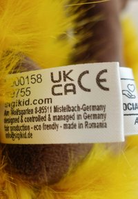 Fluffy yellow fabric label with white printing, attached to a brown textile base. Includes care instructions and manufacturer details.