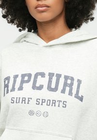 Ανοιχτό γκρι φούτερ με καγκουρό τσέπη, με φθαρμένο μπλε γραφικό "RIPCURL" και "SURF SPORTS" στο μπροστινό μέρος. Μαλακή υφή υφάσματος.