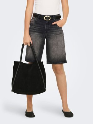 Persoon die vervaagde zwarte knielange denimshorts draagt met zwarte riem, wit topje, zwarte gevlochten platte schoenen, en een grote zwarte tas vasthoudt.