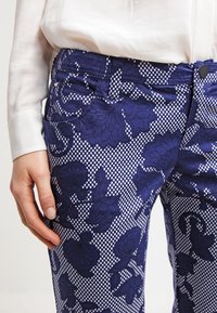 Marina byxor med blommönster i mörka nyanser på en prickig bakgrund; inkluderar fickor och knäppning.