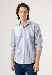Camisa de botones a rayas azul claro y blanca con un bolsillo en el pecho. Tela de algodón, mangas largas, ligera y con dobladillo redondeado.